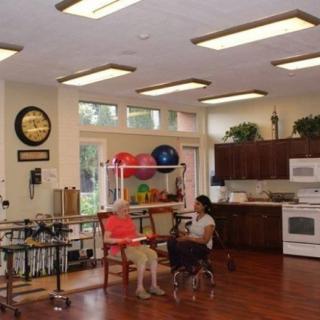 A rehabilitation room equipped with a kitchen area and exercise equipment, where two people are engaged in therapy.