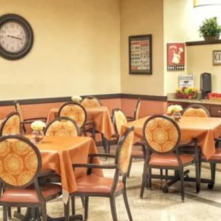 A cozy dining area with neatly arranged tables and chairs, featuring warm decor and a wall clock.