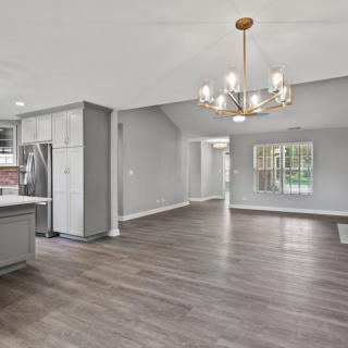 Modern open floor plan with a spacious kitchen and living area featuring hardwood floors and a stylish chandelier.