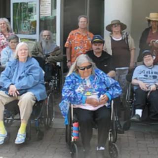 A group of seniors gathered outdoors, some using wheelchairs and wearing colorful clothing.