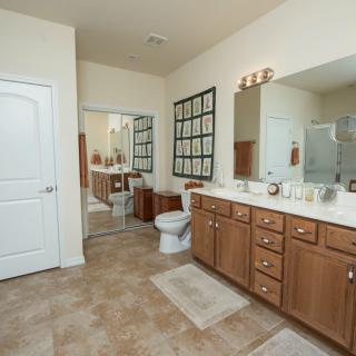 A spacious bathroom with wooden cabinets, a large mirror, and tiled flooring.