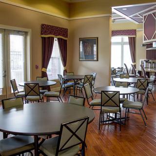 A cozy dining area with round tables and chairs, featuring wood flooring and large windows with curtains.