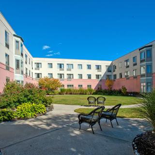 A sunny courtyard with benches, surrounded by a multi-story building and landscaped gardens.