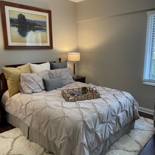 A cozy bedroom with stylish decor, featuring a neatly made bed, a bedside lamp, and framed artwork on the wall.