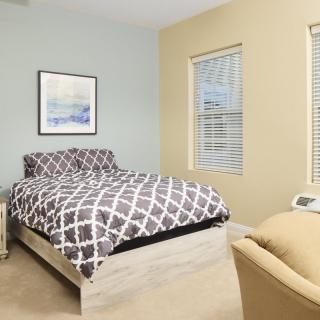 A cozy bedroom featuring a bed with patterned bedding, neutral walls, and two windows allowing natural light.