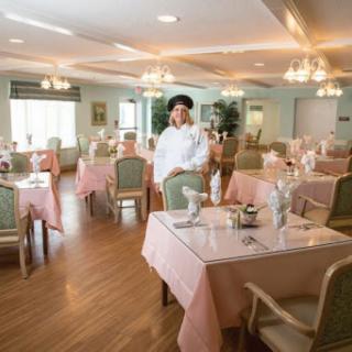 A chef stands in an elegantly set dining area, ready to serve.