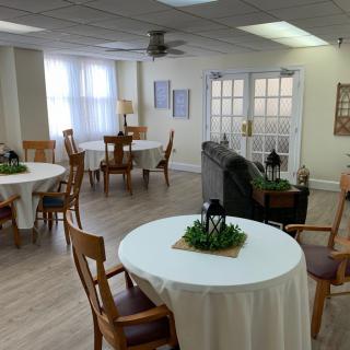 A cozy dining room with round tables and wooden chairs, decorated with small potted plants, illuminated by natural light.