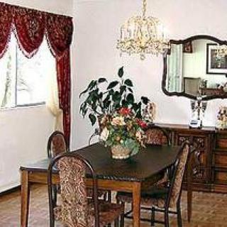 A classic dining room with a dark wooden table, patterned chairs, a chandelier, and decorative elements like flowers and a mirror.