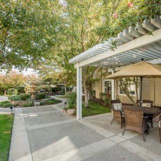 A serene outdoor patio area with a pergola and garden furniture, surrounded by trees and greenery.