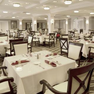 An elegant restaurant dining room with neatly arranged tables and chairs, featuring white tablecloths and a formal setting.