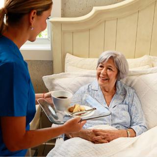 A nurse serves breakfast to an elderly woman in bed, providing care and support.