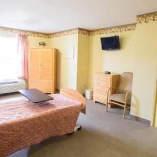 A simple, well-lit hospital room featuring a bed, chair, and television.