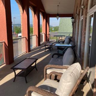 A sunny balcony with comfortable outdoor seating and tables.