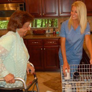 A caregiver assisting an elderly woman in the kitchen.