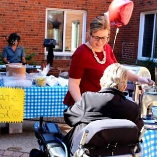 A community event where a woman assists an elderly person while others enjoy the festivities in the background.