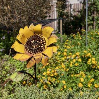 A garden with a metal sunflower sculpture surrounded by yellow flowers.