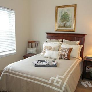 A cozy bedroom with a neatly made bed, decorative pillows, and a painting above the headboard.