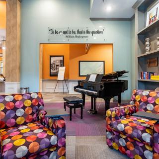 A vibrant music room featuring a grand piano, colorful chairs, and an inspirational quote on the wall.