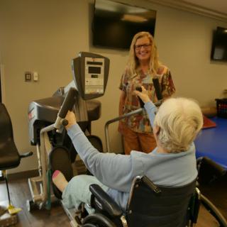 A healthcare professional assists an elderly patient using exercise equipment during a rehabilitation session.