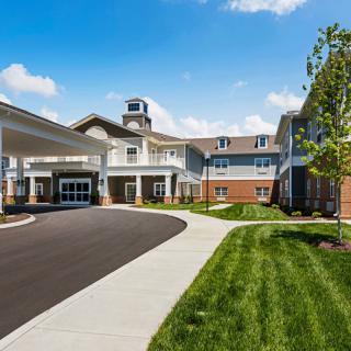 A modern residential building with a driveway and landscaped surroundings under a clear blue sky.