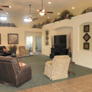 A spacious and well-decorated living room featuring comfortable seating, ceiling fans, and a television.