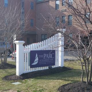 A sign for 'The Parc at Harbor View' situated in front of a building, surrounded by trees and grass.
