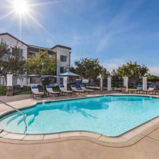 A sunny day by the outdoor swimming pool with deck chairs in front of a residential building.