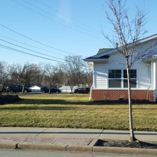 A view of a residential building with a neatly maintained lawn, a small tree in front, and clear blue skies.