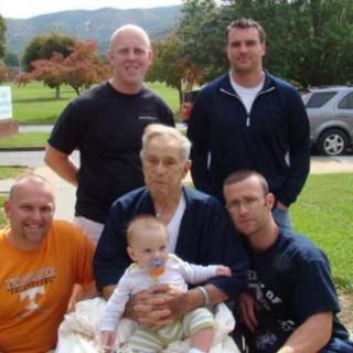 A family group photo taken outdoors with an elderly person and a baby.