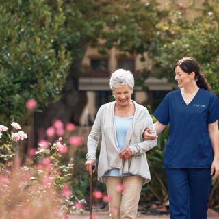A nurse walking alongside an elderly woman in a garden.