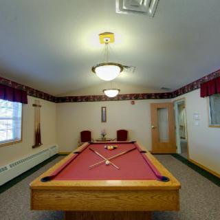 A recreation room featuring a red pool table with two chairs and warm lighting.