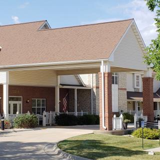 A well-maintained building entrance with columns, surrounded by greenery under a clear sky.