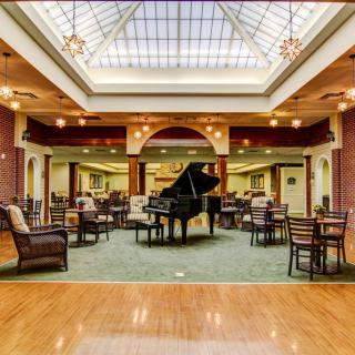 A luxurious lounge area featuring a grand piano, surrounded by comfortable seating and illuminated by an ornate skylight.