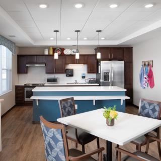 A modern kitchen with a central island and dining area, featuring pendant lighting and stainless steel appliances.