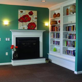 A cozy living room with a fireplace, built-in bookshelf, and green walls adorned with floral artwork.