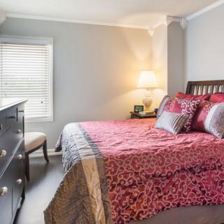 A cozy bedroom with elegant bedding, a lamp, and a dresser.