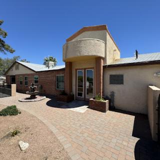 A welcoming entrance to a modern adobe-style home, surrounded by landscaped pathways under a clear blue sky.