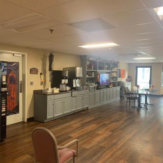 A cozy common area with a kitchen setup, featuring a coffee machine and seating.