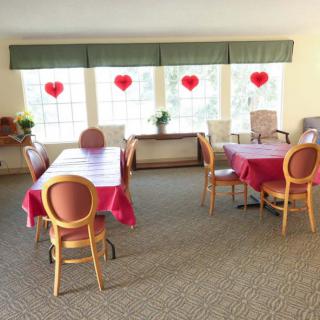 A dining room with tables covered in red tablecloths and heart decorations on the windows.