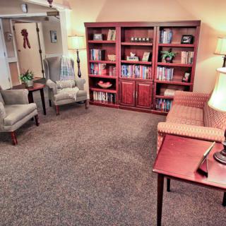 A cozy living room with bookshelves, comfortable chairs, a sofa, and warm lighting.