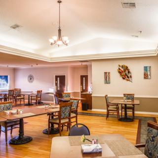 A spacious dining room with wooden flooring, featuring multiple tables and chairs, adorned with a chandelier and artistic wall decorations.