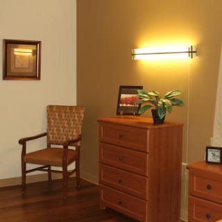 A cozy corner of a room featuring a wooden dresser, a comfortable chair, and soft lighting.