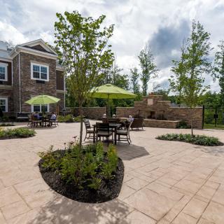 A well-landscaped outdoor patio area with tables, chairs, and umbrellas near a residential building.