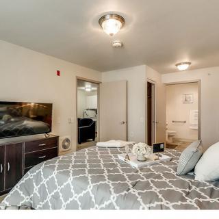 A modern bedroom featuring a neatly made bed, a TV on a dresser, and contemporary lighting fixtures.