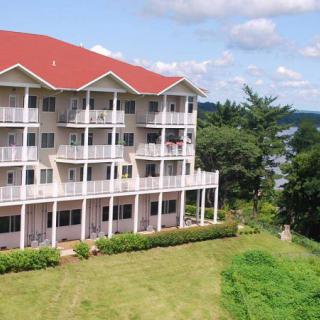 A multi-story apartment building with balconies surrounded by greenery and a clear sky.