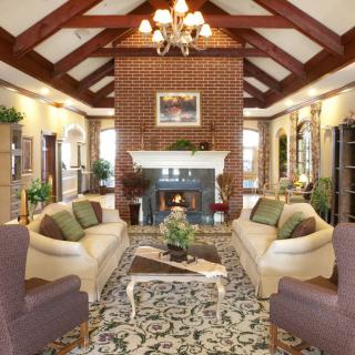 A luxurious living room featuring a central fireplace, elegant sofas, armchairs, and a decorative rug under a vaulted ceiling with an ornate chandelier.