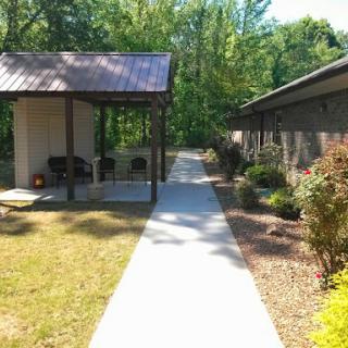 A serene pathway leading through a landscaped area, showcasing a pavilion and nearby building in a natural setting.