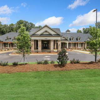 A modern building with a prominent entrance surrounded by landscaped greenery and a clear blue sky.