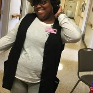 A person smiling and posing in a hallway wearing casual clothing.