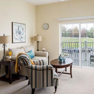 A cozy living room with a sofa, armchair, and coffee table, featuring a large balcony door bringing in natural light.